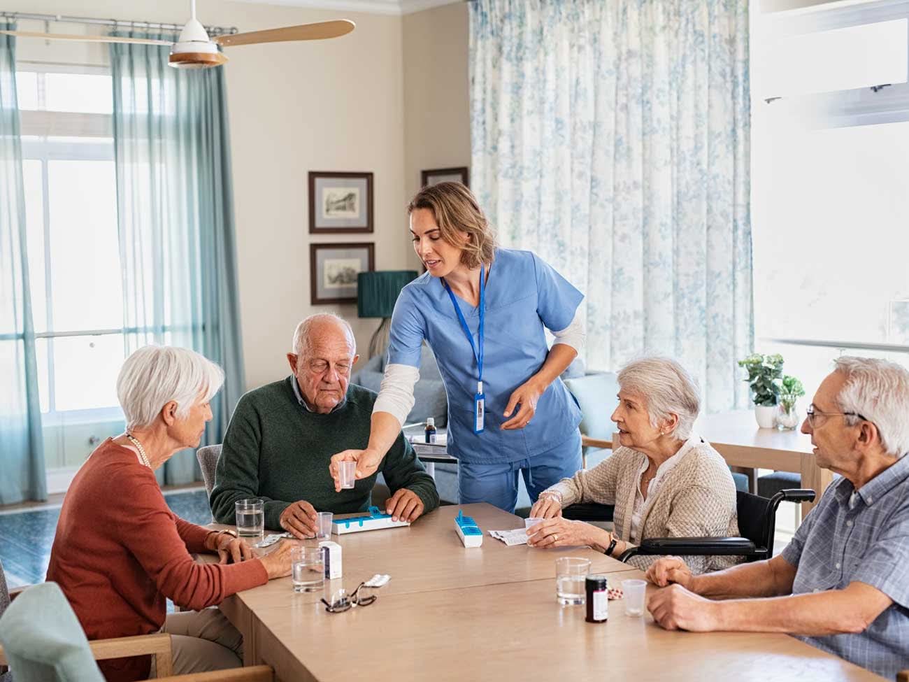 Nurse distributes medication to seniors around a table.