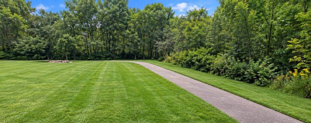 Curving paved path beside manicured lawn and wooded greenery at Evera at Rosemount