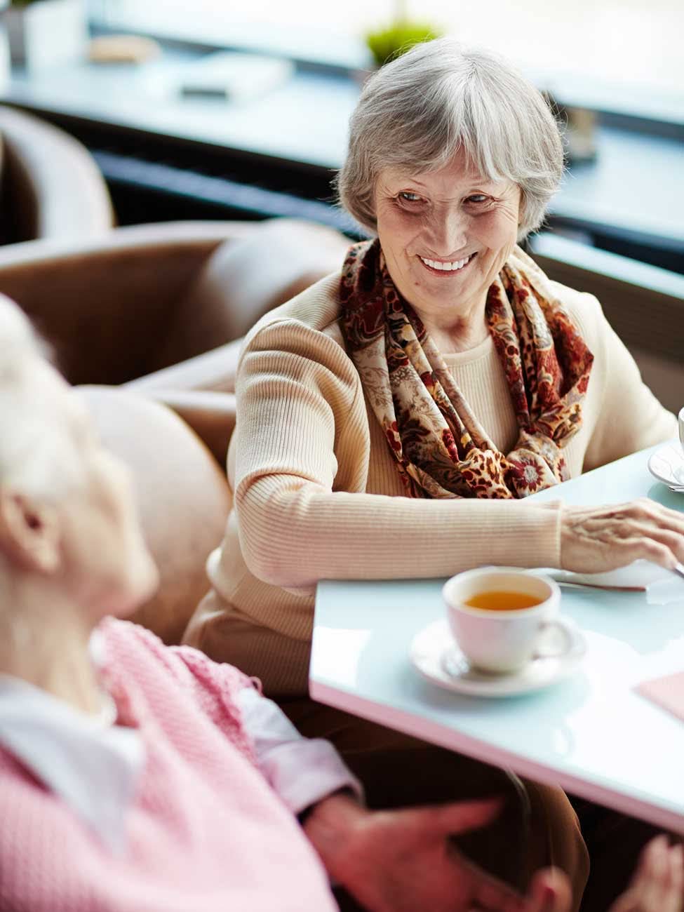 Smiling elderly woman enjoys tea with a friend at cafe